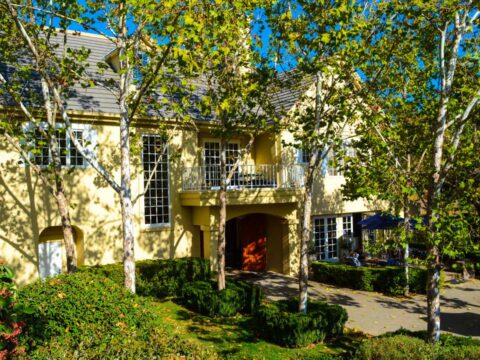 Yellow two-story house surrounded by leafy trees