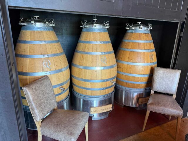 Three large wooden fermentation barrels with chairs indoors